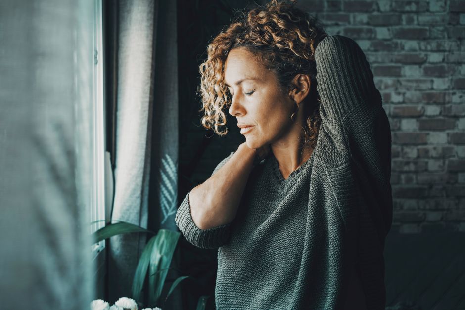 woman in pain next to window looking sad